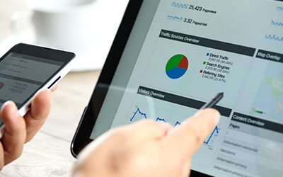 Hands hold a smartphone and a tablet displaying web traffic data graphs